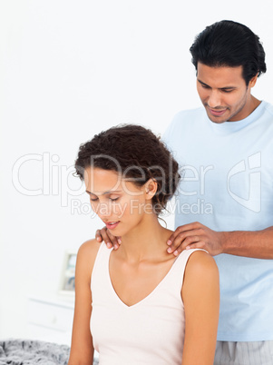 Hispanic man massaging his girlfriend sitting on their bed