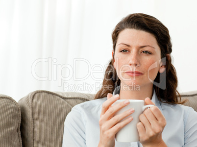 Thoughtful woman drinking coffee on the sofa