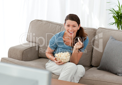 Merry woman eating pop corn while watching a movie on television