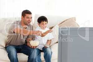 Happy father and son watching television while eating pop corn