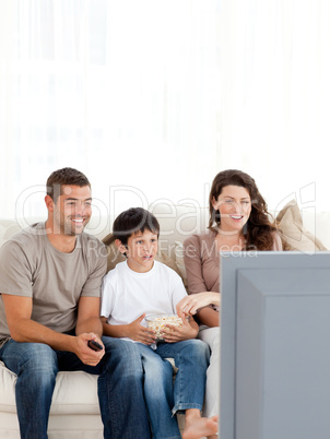 Happy family watching television while eating popcorn together