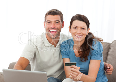 Cute couple with their laptop and credit card sitting in the liv