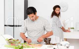 Concentrated man cutting vegetables with his girlfriend