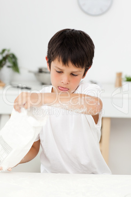 Cute boy pouring flour on a table in his kitchen