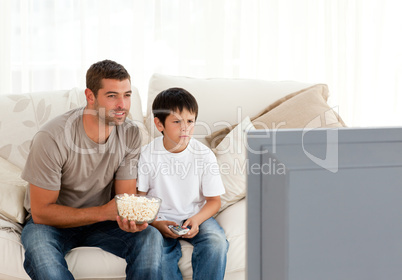 Concentrated father and son watching television while eating pop