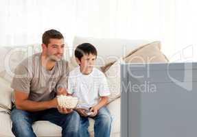 Concentrated father and son watching television while eating pop