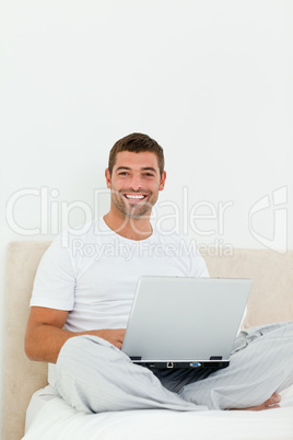 Cheerful man working on his laptop sitting on his bed