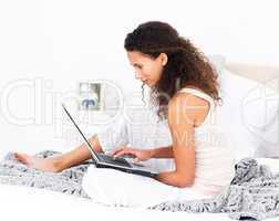 Pretty woman working on her laptop on her bed