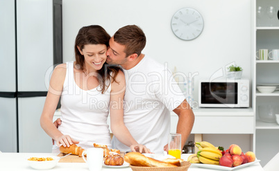 Affectionate man kissing his girlfriend while cutting bread for