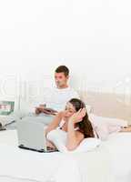 Pretty woman working on her laptop while her husband is reading
