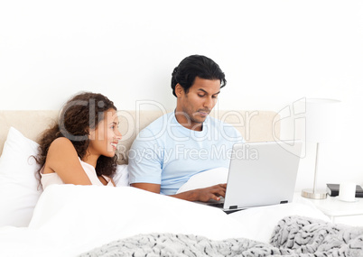 Happy woman looking her husband working on his laptop on the bed