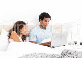 Happy woman looking her husband working on his laptop on the bed