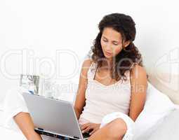Cute woman working on her laptop sitting on her bed