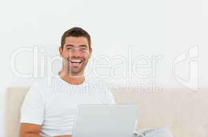 Happy man working on his laptop in his bedroom