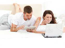 Cute couple working together on their laptop lying on their bed
