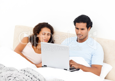 Serious man working on his laptop lying on his bed