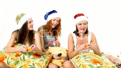 Young girls in santa hat eat mandarin on pillows - christmas theme