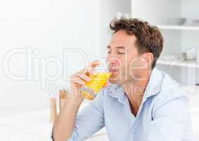 Handsome man enjoying his orange juice sitting in the kitchen
