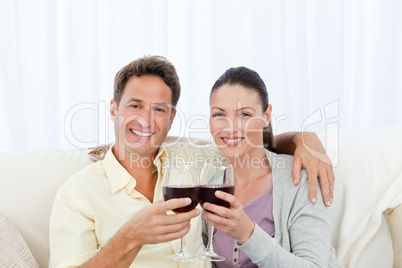 Portrait of a couple clinking glasses of red wine on the sofa