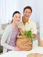 Couple laughing standing in the kitchen with shopping bags
