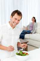 Happy man preparing lunch while his girlfriend relaxing