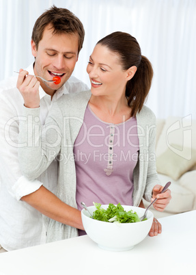 Pretty woman giving a tomato to his boyfriend while preparing a