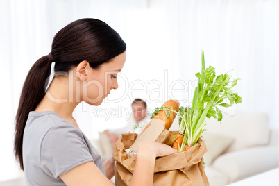 Man relaxing on the sofa while his girlfriend tidying the kitche