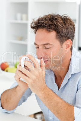 Handsome man smelling his coffee sitting in his kitchen