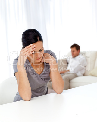 Worried woman sitting at a table while her boyfriend is lying on
