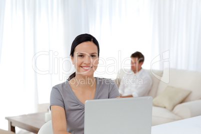 Cute woman working on the laptop while her husband relaxing