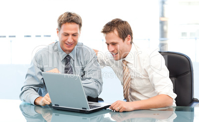 Two happy businessmen working together on a laptop sitting at a