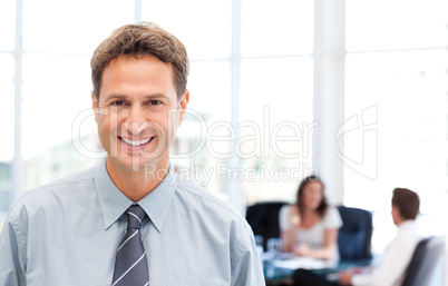 Happy businessman in the foreground while his team is working