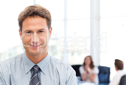 Relaxed businessman posing in front of his team while working in