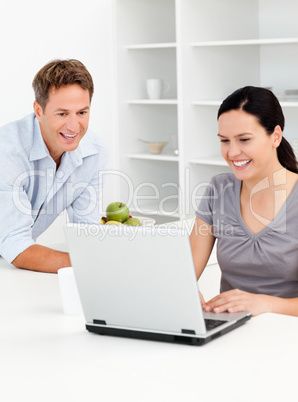 Happy couple looking at their laptop while drinking coffee
