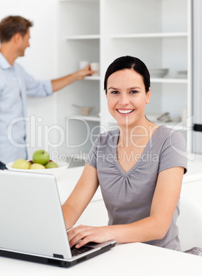 Happy woman working on the laptop in the kitchen with her boyfri