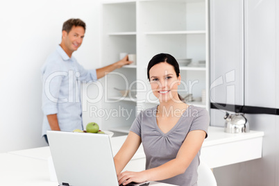Happy woman on the laptop while her husband preparing coffee
