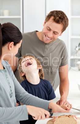 Little boy laughing while his mother cutting bread