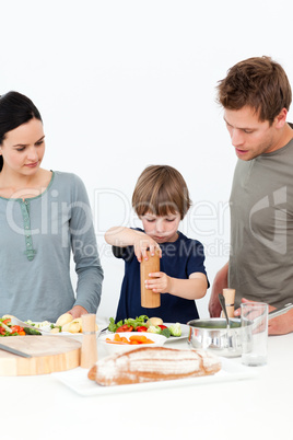 Cute boy putting salt and pepper in his salad in the kitchen