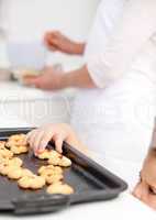 Cute little girl taking cookies while her mother is cooking