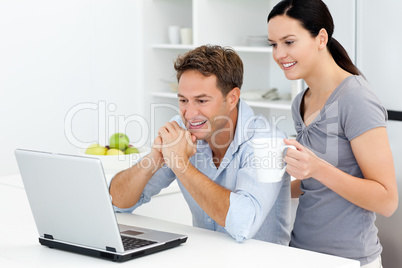 Happy couple looking at something on the laptop while drinking c