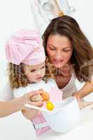 Mother and daughter breaking eggs while cooking