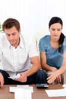 Desperate couple looking at their bills sitting on the sofa