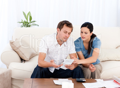 Man showing a bill to his girlfriend sitting on the sofa