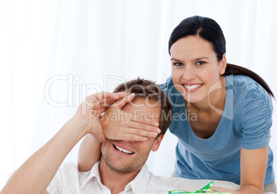 Cute woman giving a present to her bofriend relaxing on the sofa