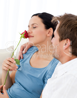 Lovely wwoman smelling a rose sitting on the sofa
