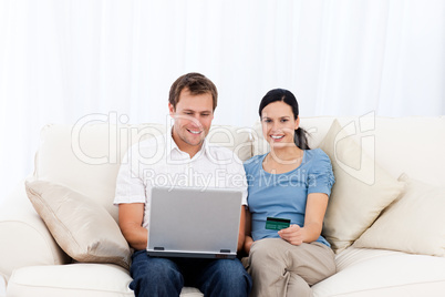 Happy couple buying online with laptop and credit card on the so