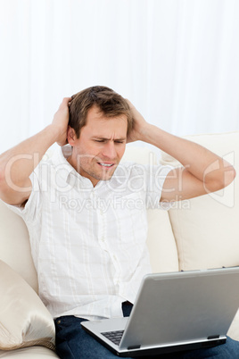Tense man working on his laptop sitting on the sofa