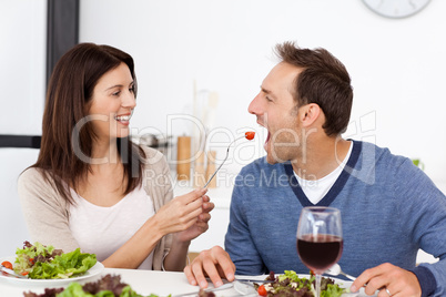 Pretty woman giving a tomato to her boyfriend while having lunch