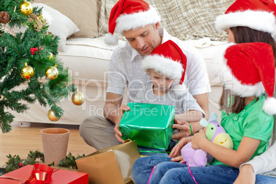 Happy family looking at the little boy opening a christmas prese