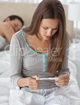 Worried woman looking a pregnancy test while her boyfriend sleep